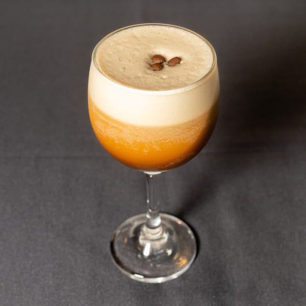 Espresso martini in a stemmed glass, topped with foam and three coffee beans on a dark surface.