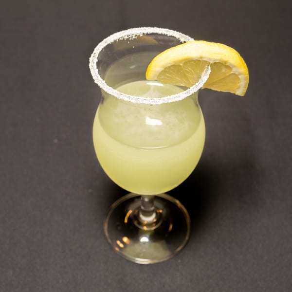 A light yellow cocktail in a stemmed glass with a sugared rim and a lemon slice.