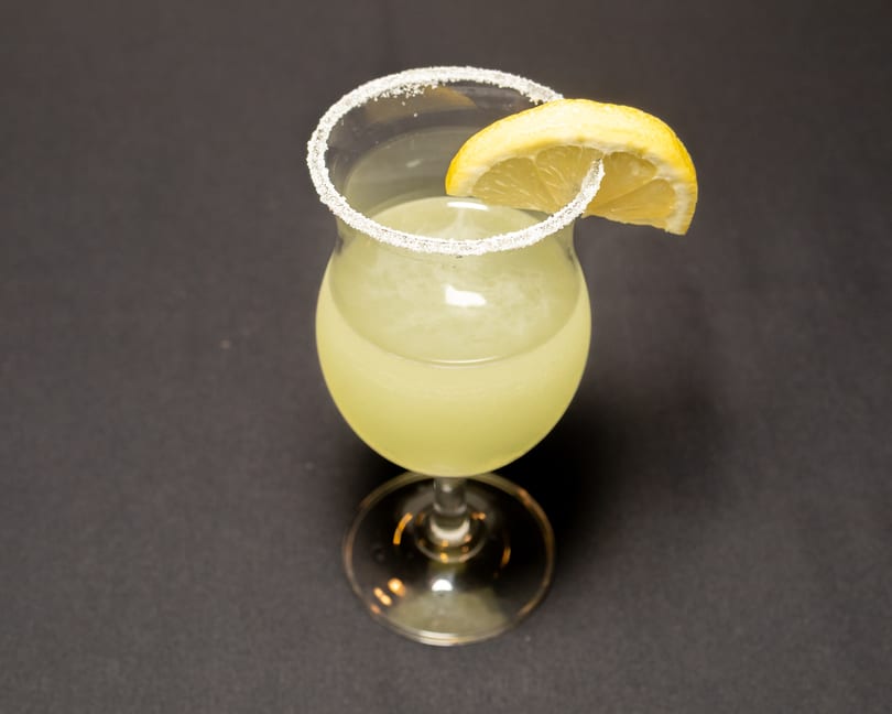 A light yellow cocktail in a stemmed glass with a sugared rim and a lemon slice.