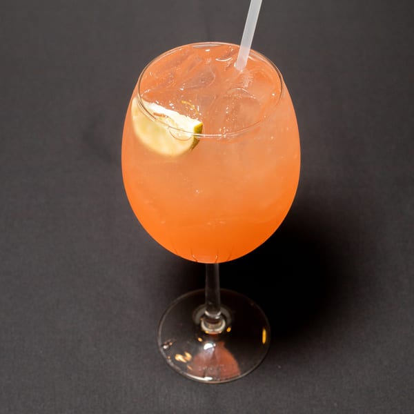 A vibrant orange cocktail with ice and a lime wedge, served in a stemmed glass on a dark surface.