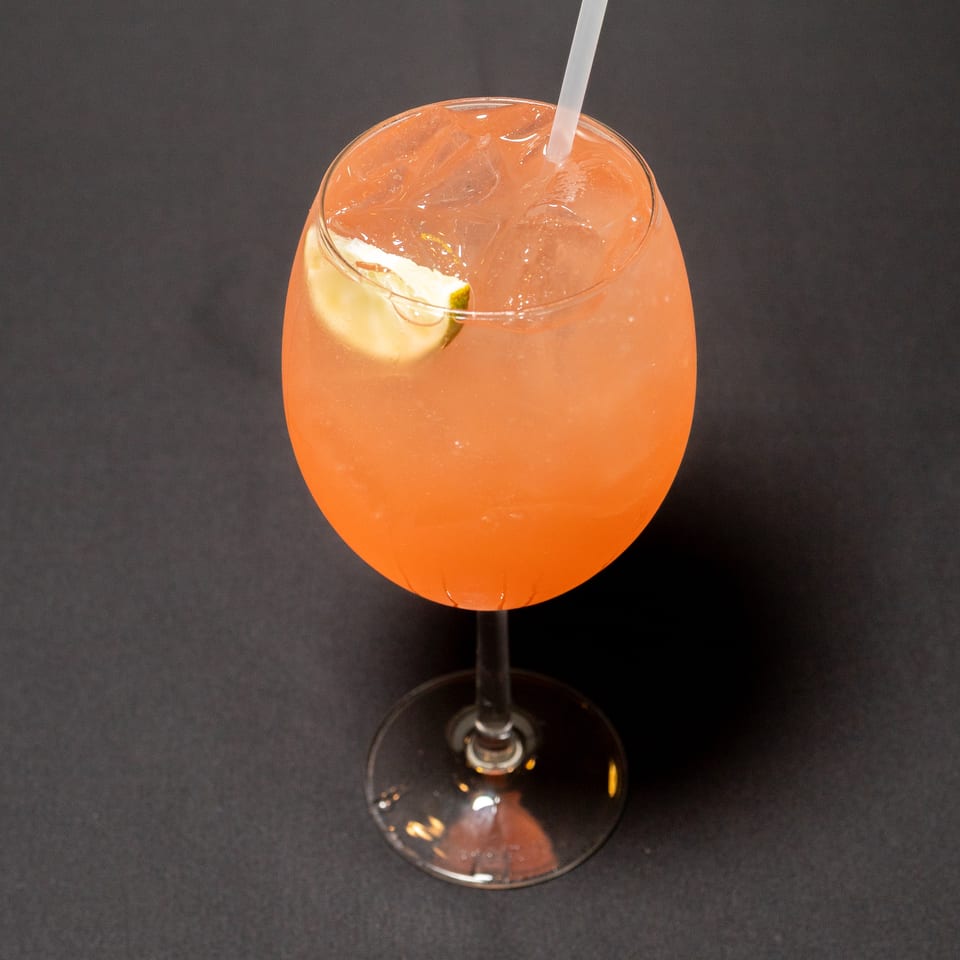A vibrant orange cocktail with ice and a lime wedge, served in a stemmed glass on a dark surface.
