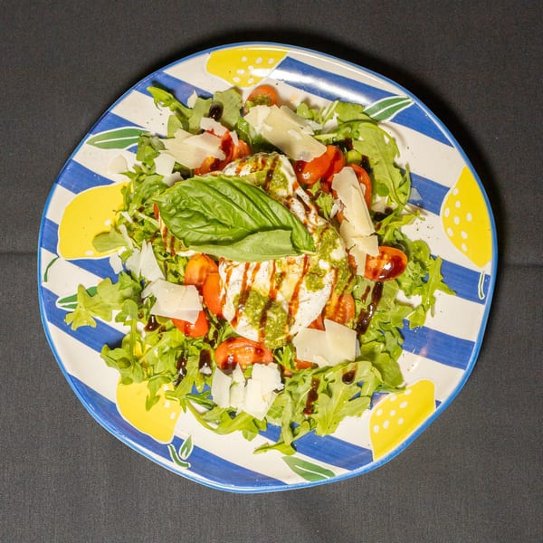 Burrata salad with arugula, cherry tomatoes, pesto, balsamic glaze, and parmesan on a striped plate.