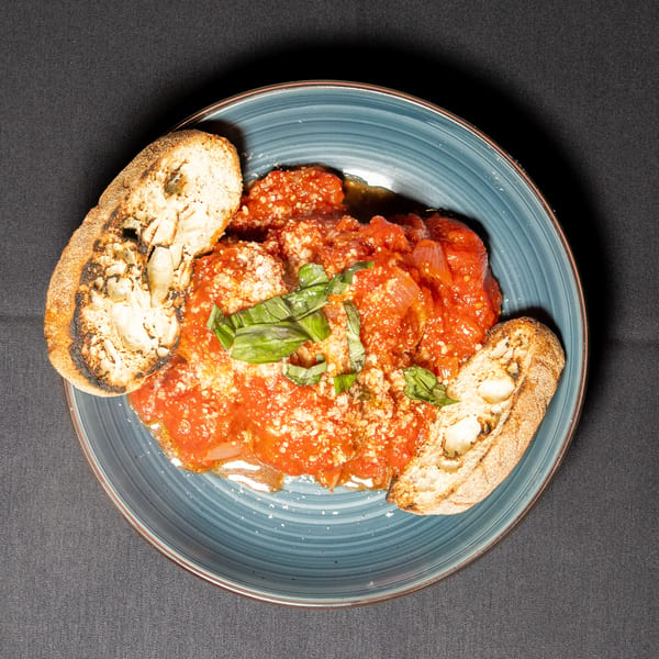 Meatballs in red sauce with parmesan cheese, basil, and toasted bread on a blue plate.