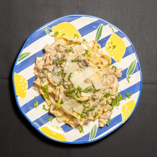 Creamy pasta with mushrooms, ground meat, parsley, and parmesan cheese on a lemon-patterned plate.