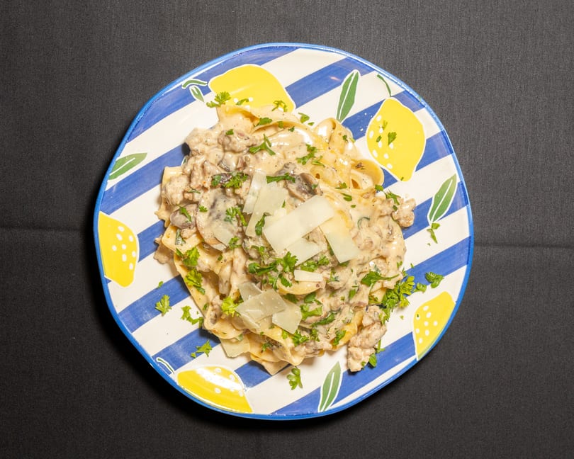 Creamy pasta with mushrooms, ground meat, parsley, and parmesan cheese on a lemon-patterned plate.