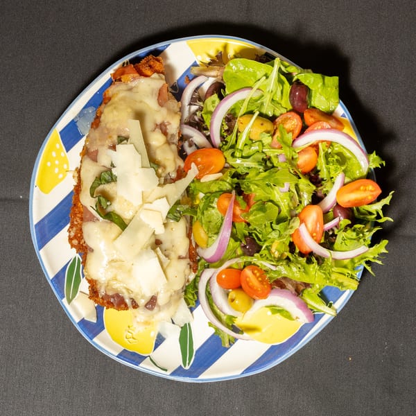 Chicken parmesan with melted cheese and basil, served with a fresh green salad.