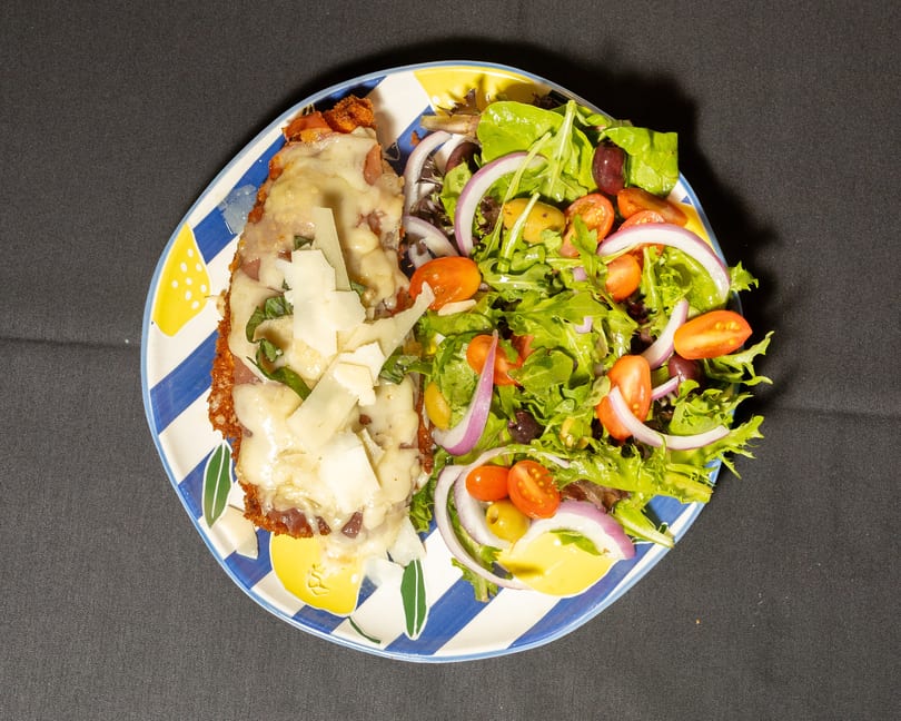 Chicken parmesan with melted cheese and basil, served with a fresh green salad.