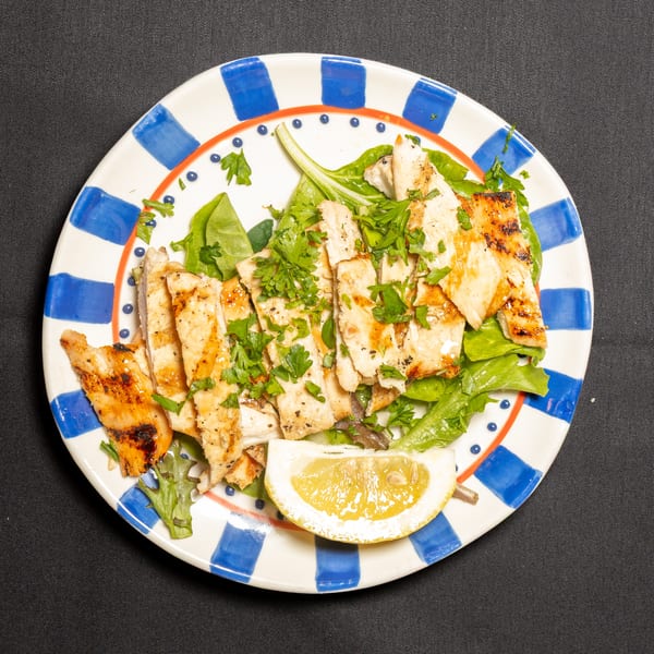 Grilled chicken strips with fresh parsley and a lemon wedge on a bed of greens.