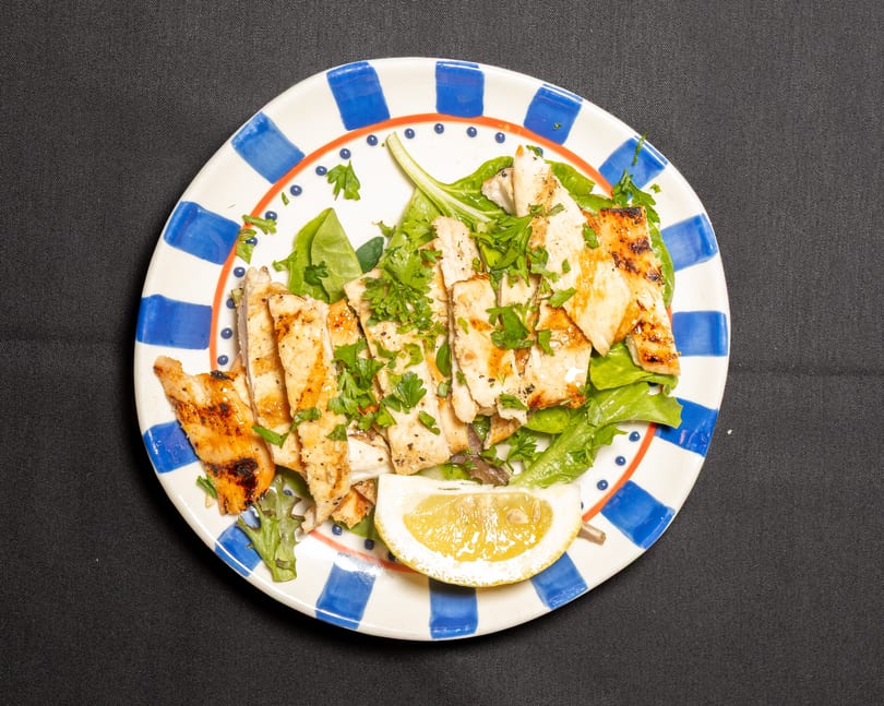 Grilled chicken strips with fresh parsley and a lemon wedge on a bed of greens.