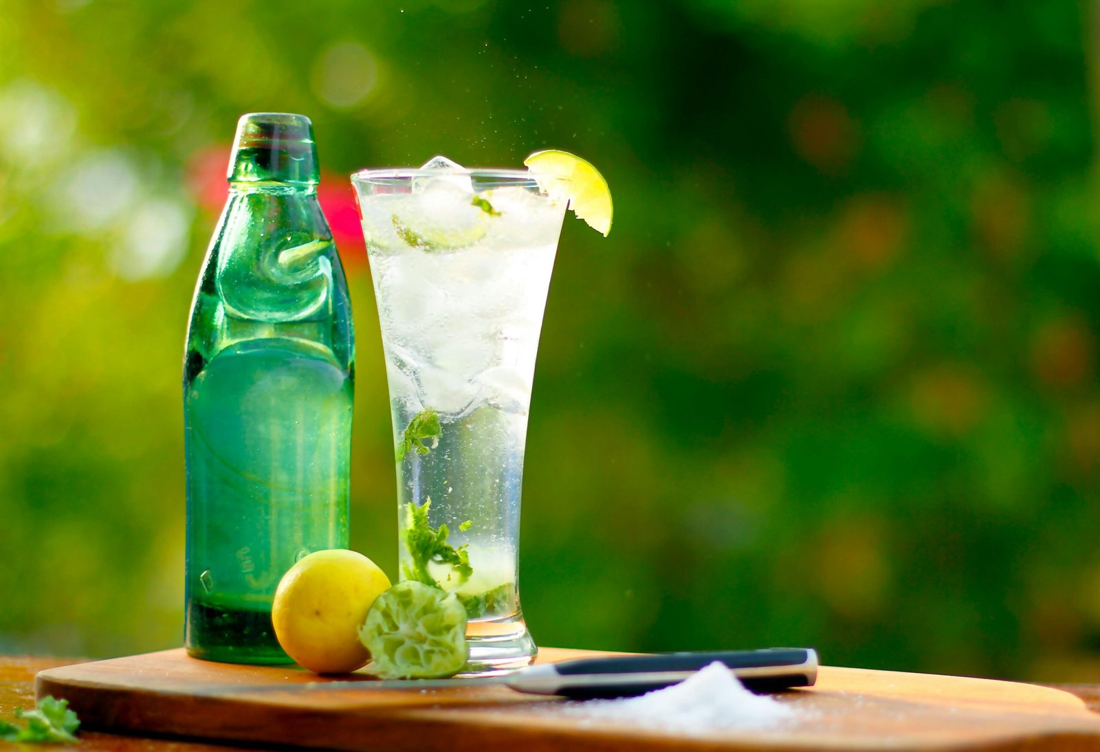 A tall glass of lime soda with ice and citrus fruits on a sunny day.